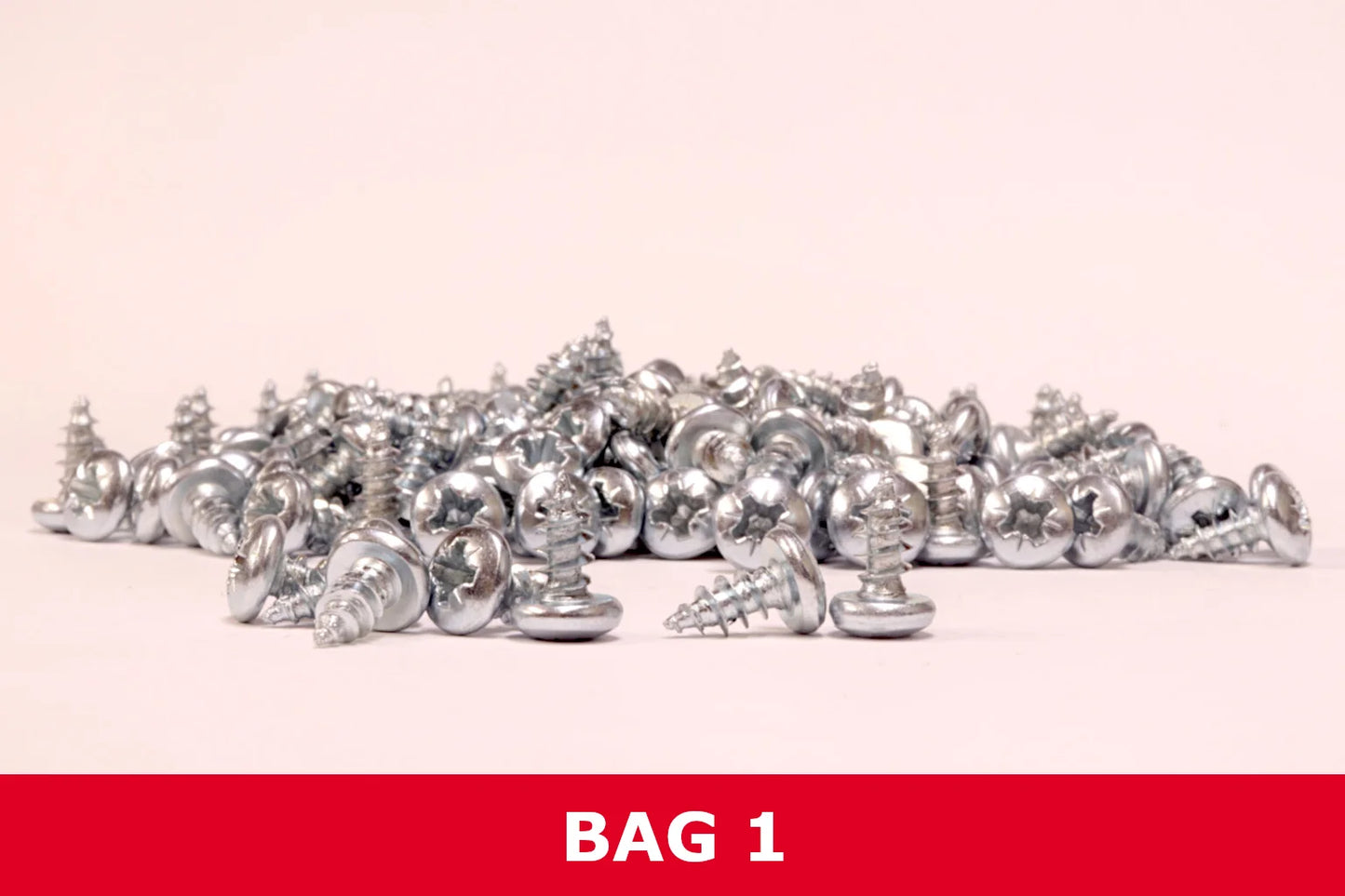 Pile of silver Phillips pan head metal screws on a plain background labeled Bag 1